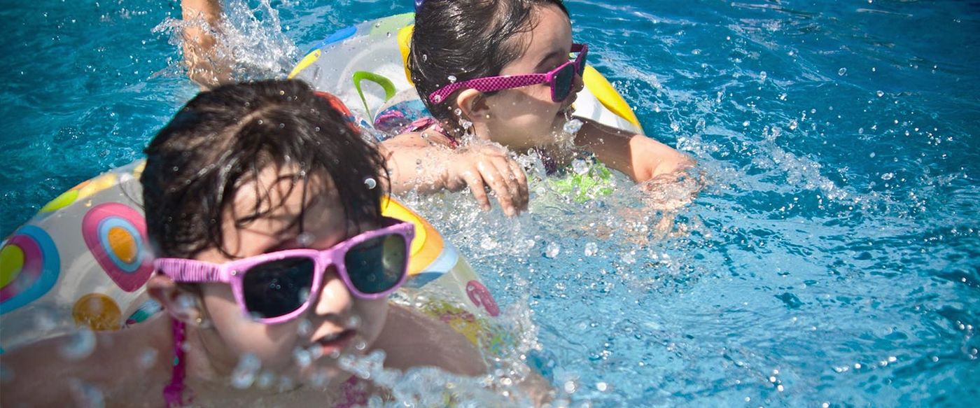 Two children swim in a pool wearing sunglasses and pool floats