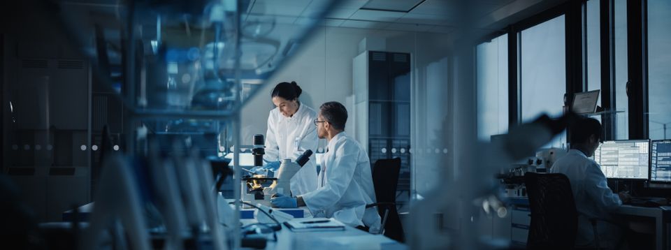 Scientists using microscopes in a research lab with colleagues working at computers nearby