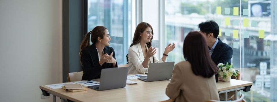 Colleagues discussing plans around a table with laptops in a meeting room