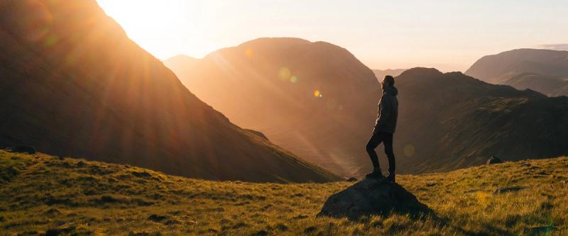 A hiker stands on a rock overlooking a mountain valley at sunrise