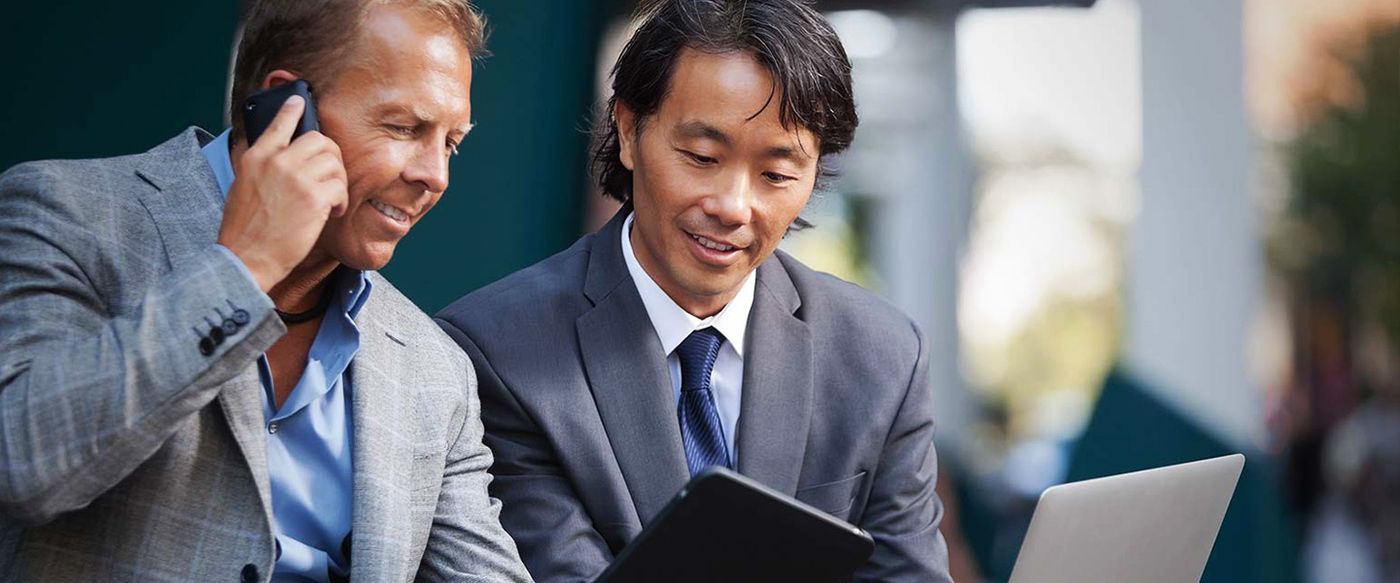 Two businessmen reviewing a tablet and laptop together outdoors