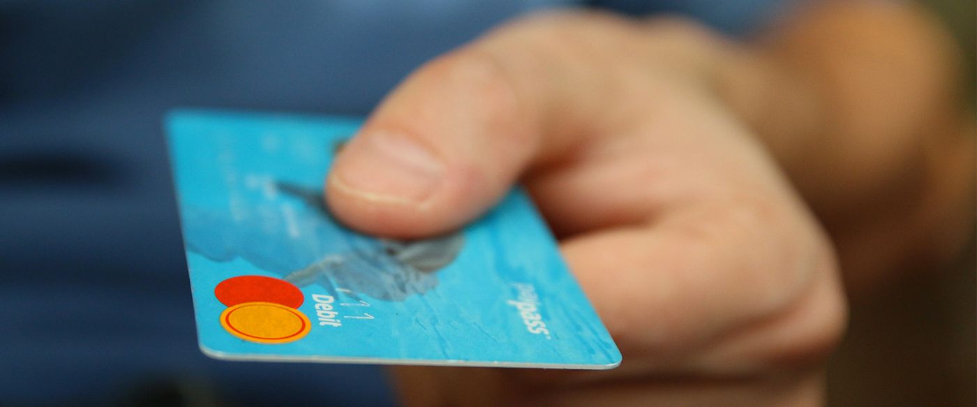 A hand holds out a blue bank card