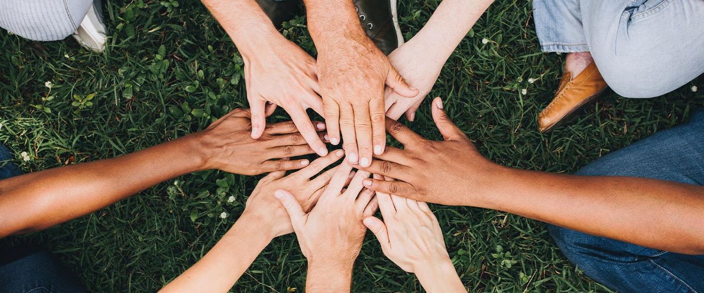 A group of people stack their hands together in a circle over grass