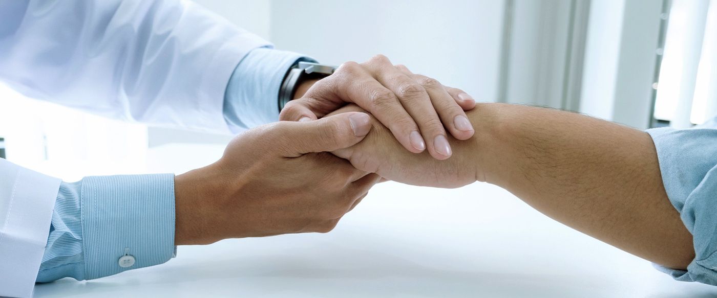 A clinician holds a patient's hand in a reassuring gesture of care
