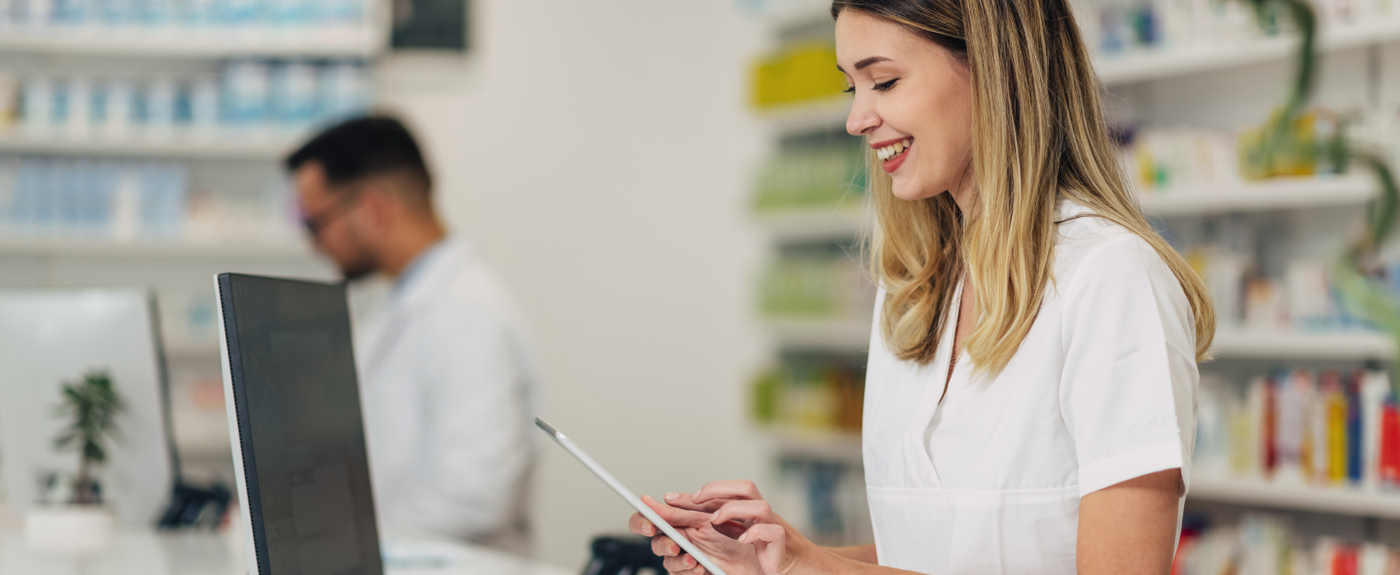 A pharmacist smiles while using a tablet at the pharmacy counter