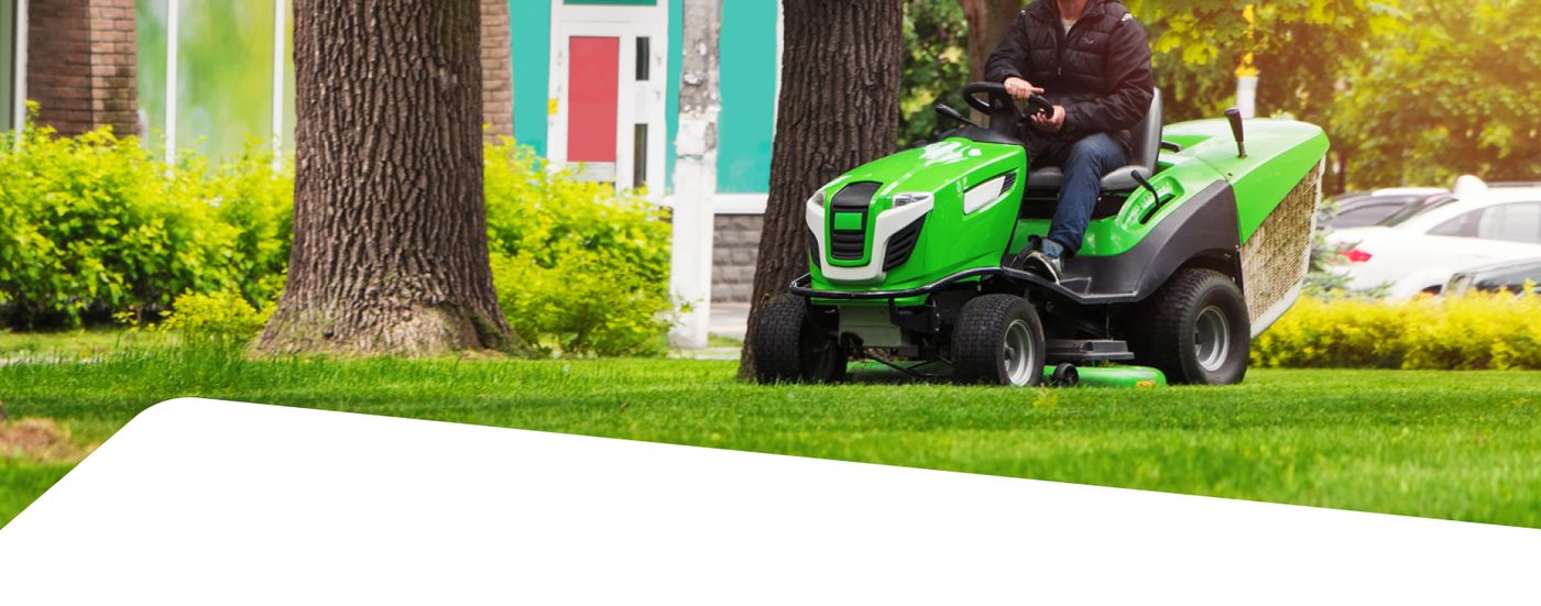 A person drives a green riding lawn mower across a grassy yard