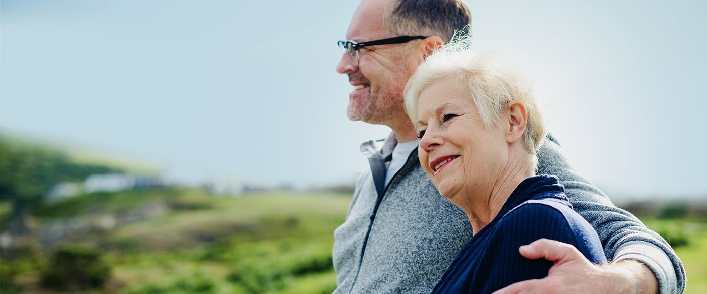 A smiling senior couple stand embracing outdoors