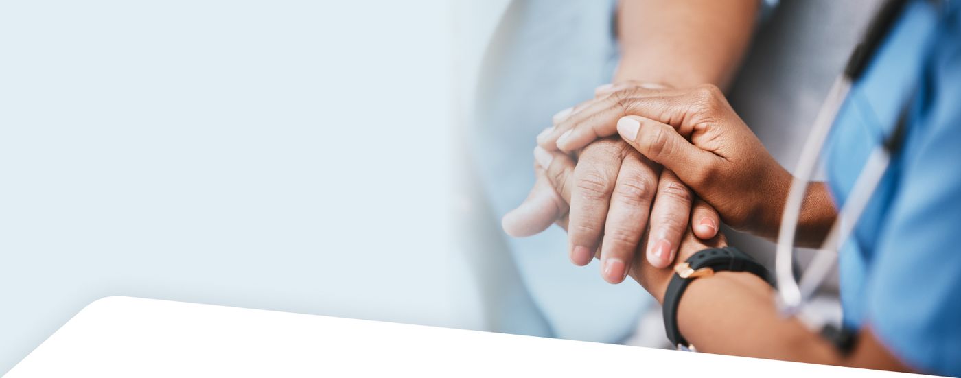 A clinician's hand rests over a patient's clasped hands in a comforting gesture