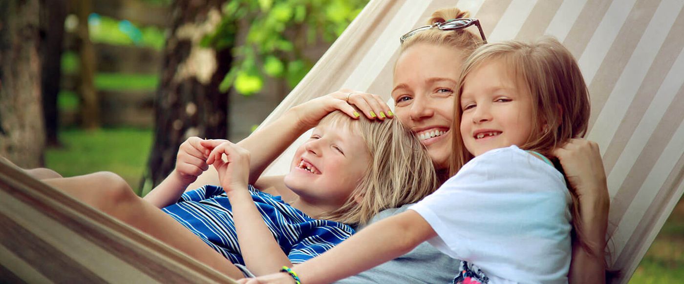 A mother laughing with her two children while relaxing together in a garden hammock