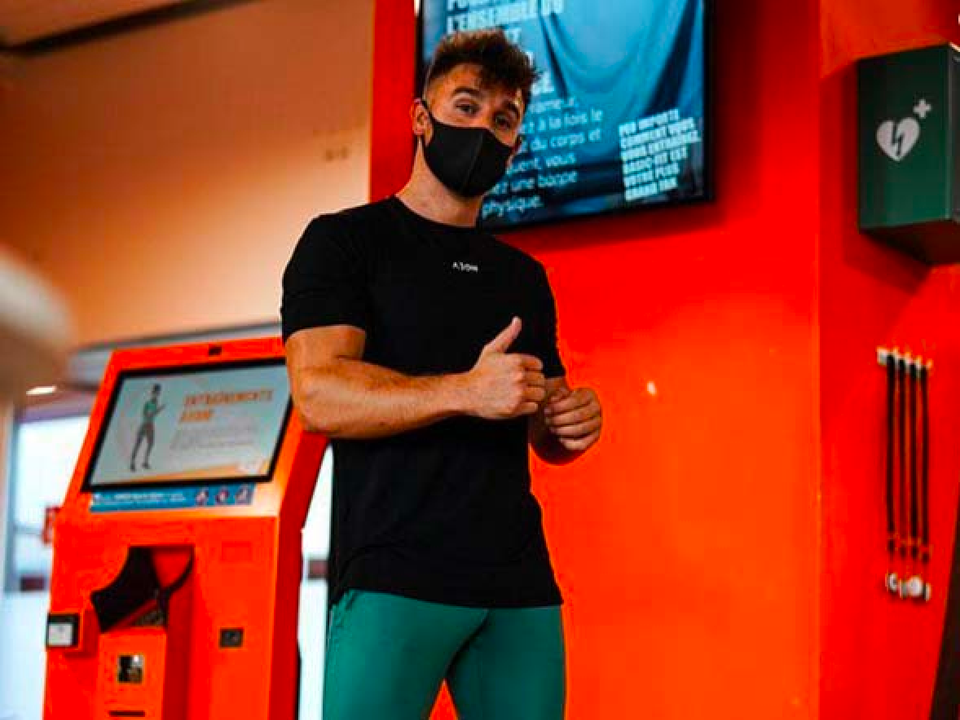 Member giving a thumbs up beside a Basic-Fit workout kiosk