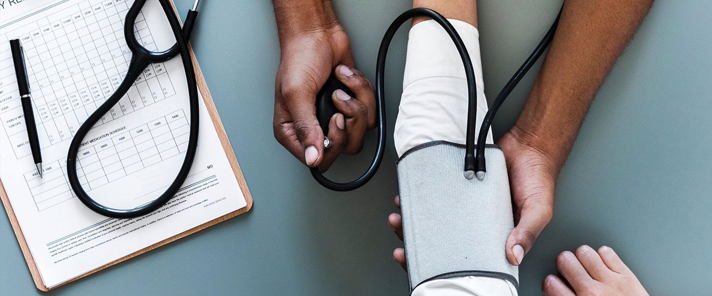 Health worker taking a patient's blood pressure beside a paper monitoring chart