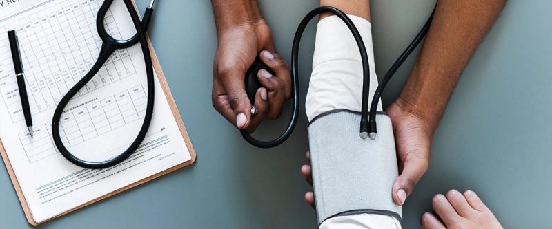 Health worker taking a patient's blood pressure beside a paper monitoring chart