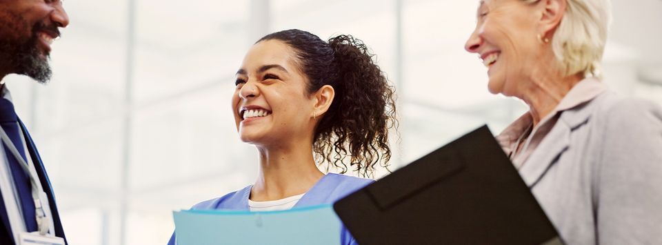 Three healthcare colleagues smiling together, one holding folders