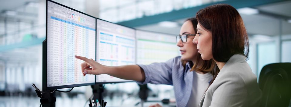 Two colleagues reviewing spreadsheet data across multiple monitors