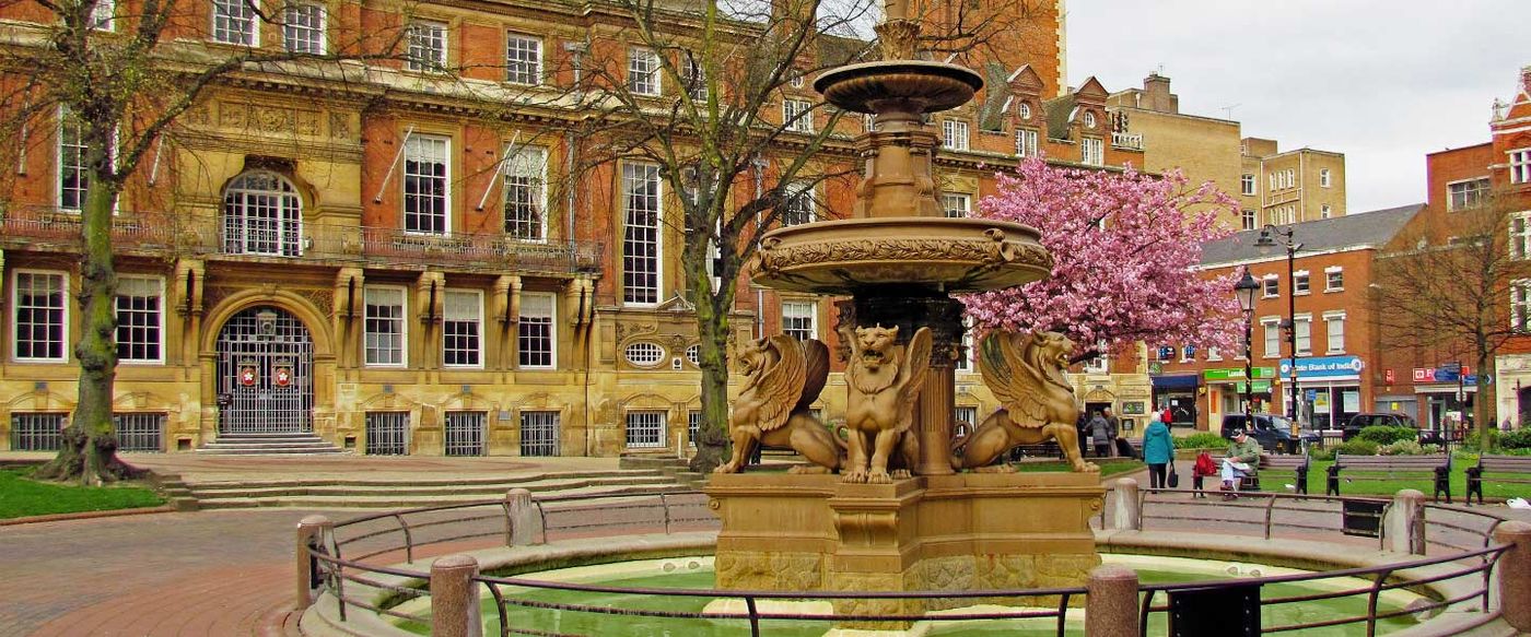 A historic town square with an ornate fountain, lions and a stately building