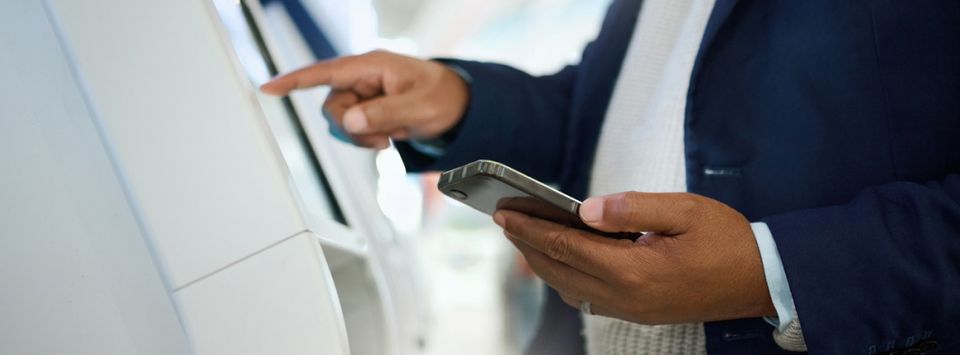 Person using a smartphone while tapping a self-service kiosk screen