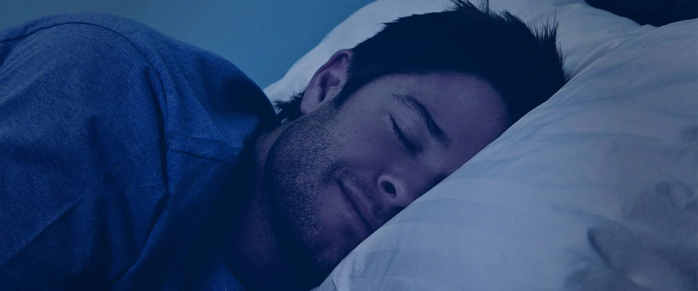 A man sleeps peacefully in a dark, calming blue-toned scene