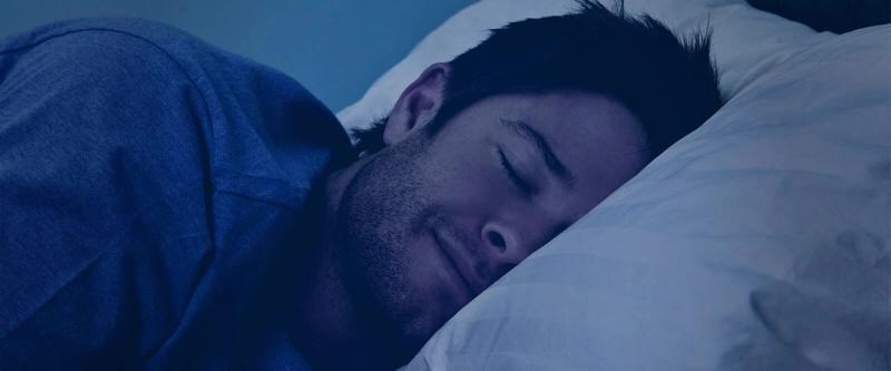 A man sleeps peacefully in a dark, calming blue-toned scene