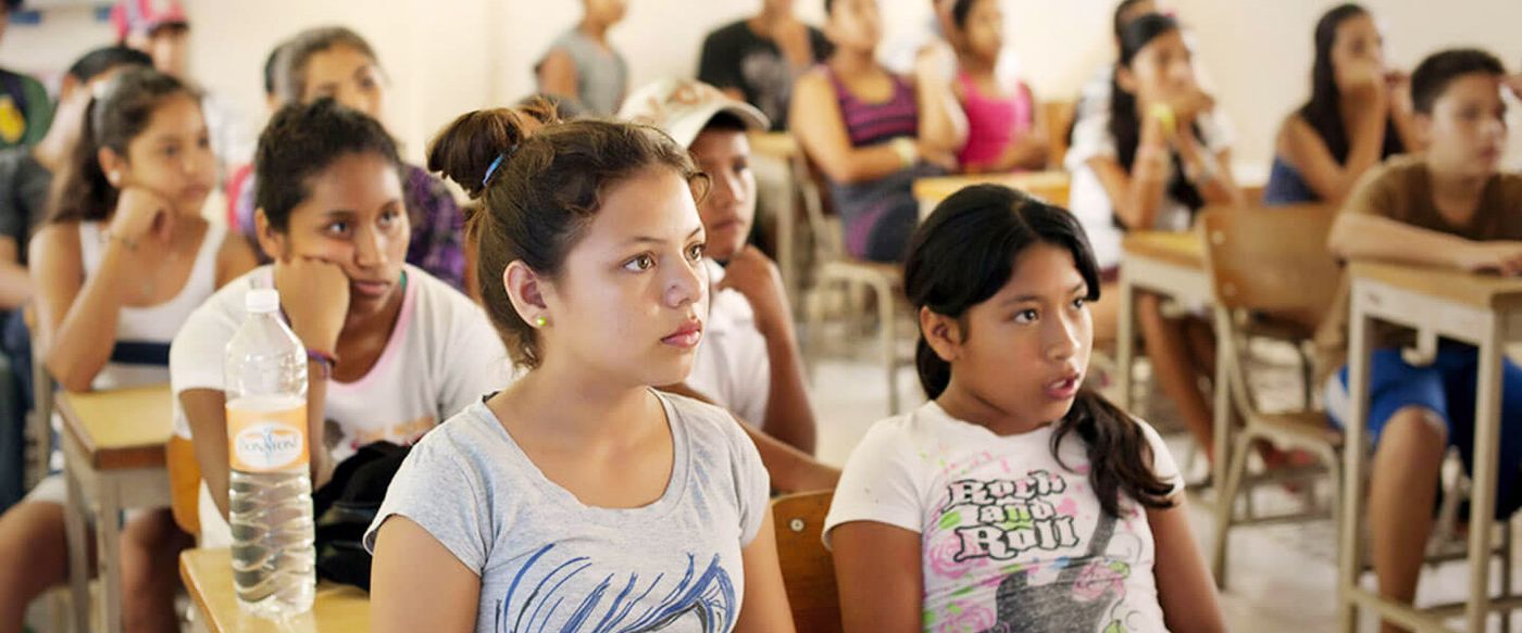 Students sit attentively at desks in a crowded classroom