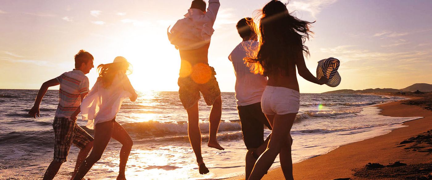 Group of friends running and jumping joyfully on a beach at sunset