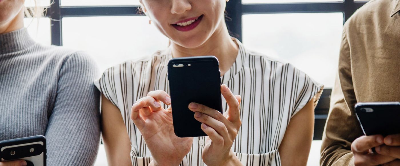 A person uses a smartphone while standing among others also on their phones