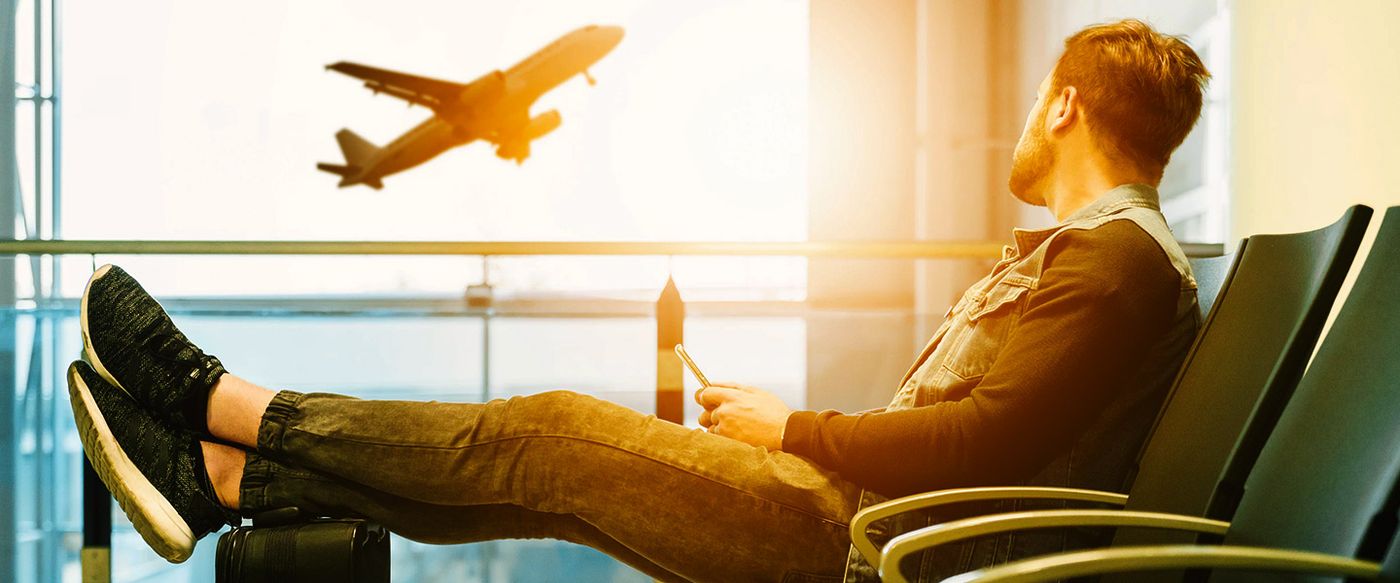 Traveler with luggage watching a plane take off from an airport lounge