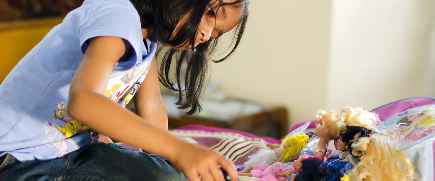 A young girl plays with dolls on her bed