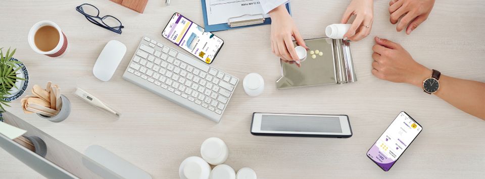Desk flatlay with a phone app, tablet, keyboard and medication blister packs