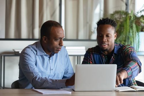 two black men in a discussion as they stare into a computer
