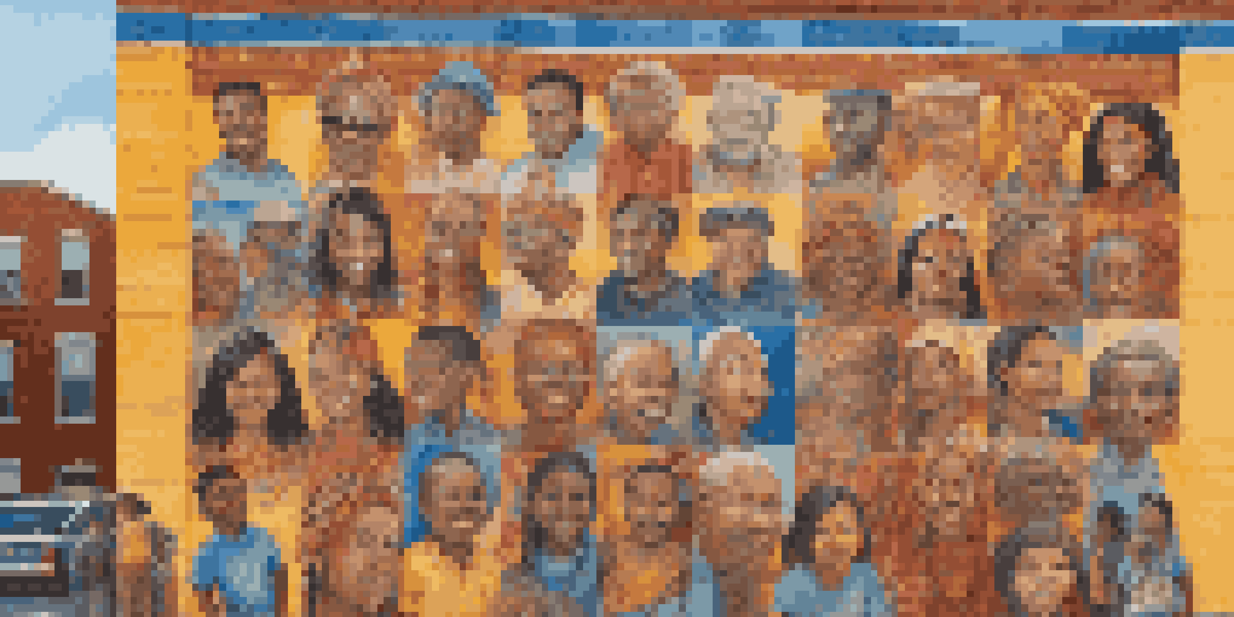 A colorful mural on a brick wall depicting diverse faces and cultural symbols, with people admiring it in a sunny setting.