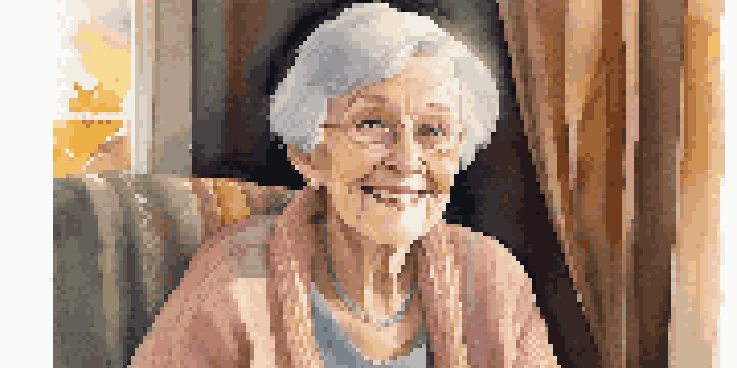 A close-up portrait of an elderly woman smiling warmly while sitting in an armchair, with soft light illuminating her features and a photo album on her lap.