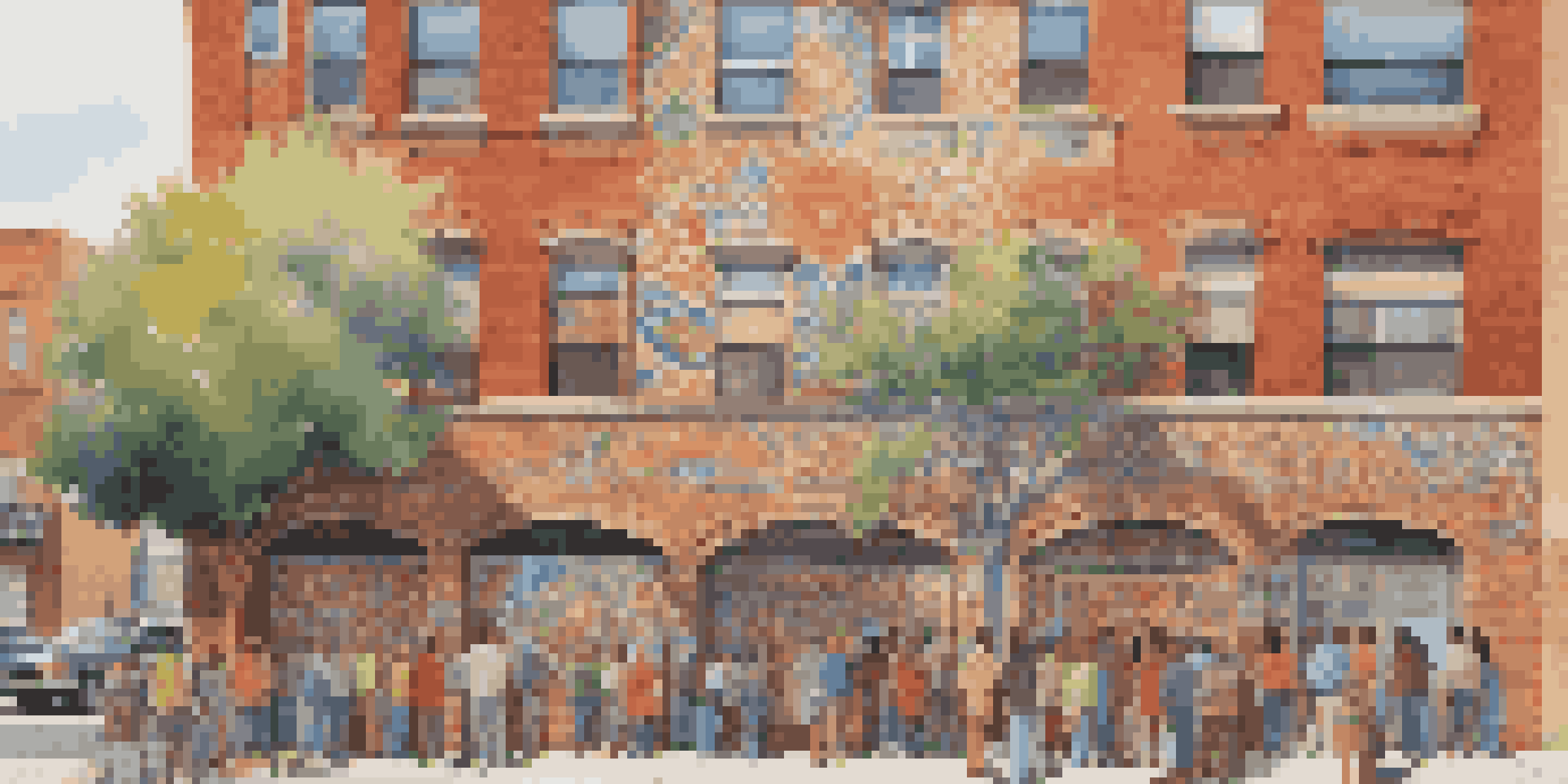 A colorful community mural on a brick wall, showcasing diverse cultural themes, with people admiring it in a lively neighborhood.
