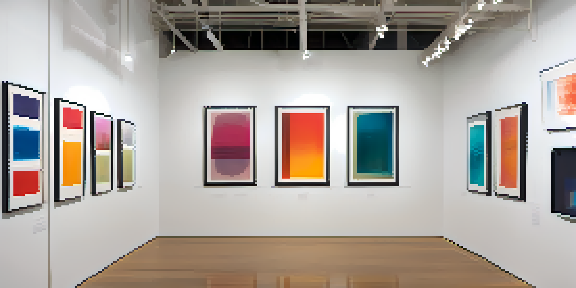 A gallery wall filled with colorful monotype prints, each displaying unique abstract designs under soft lighting.