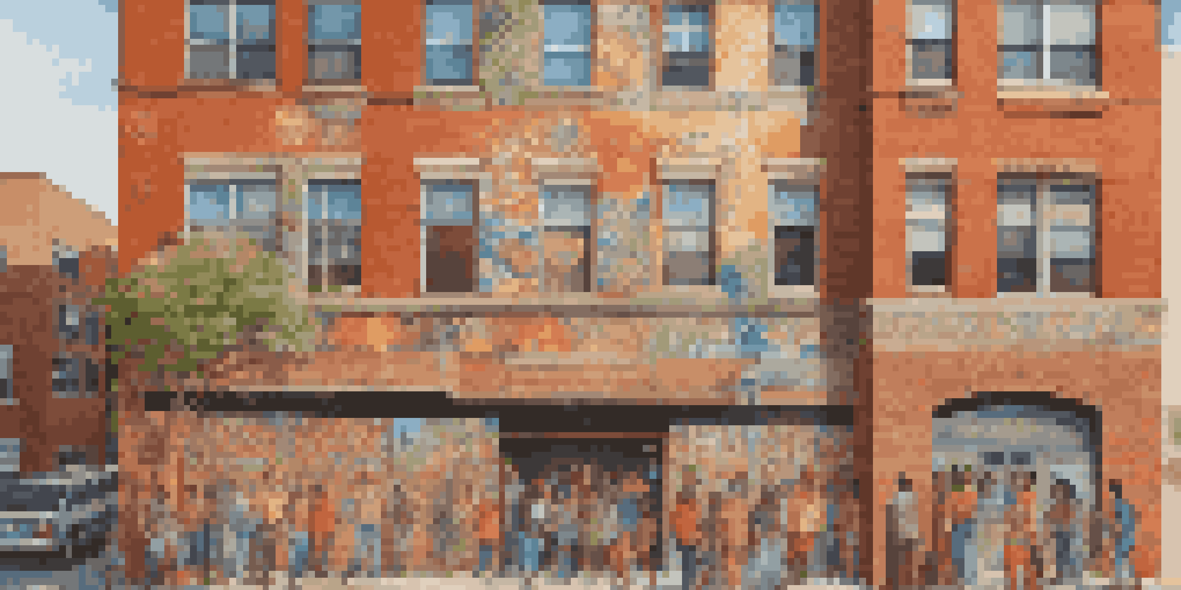 A colorful mural depicting diverse community members and cultural symbols on a brick wall in an urban area, illuminated by afternoon sunlight.