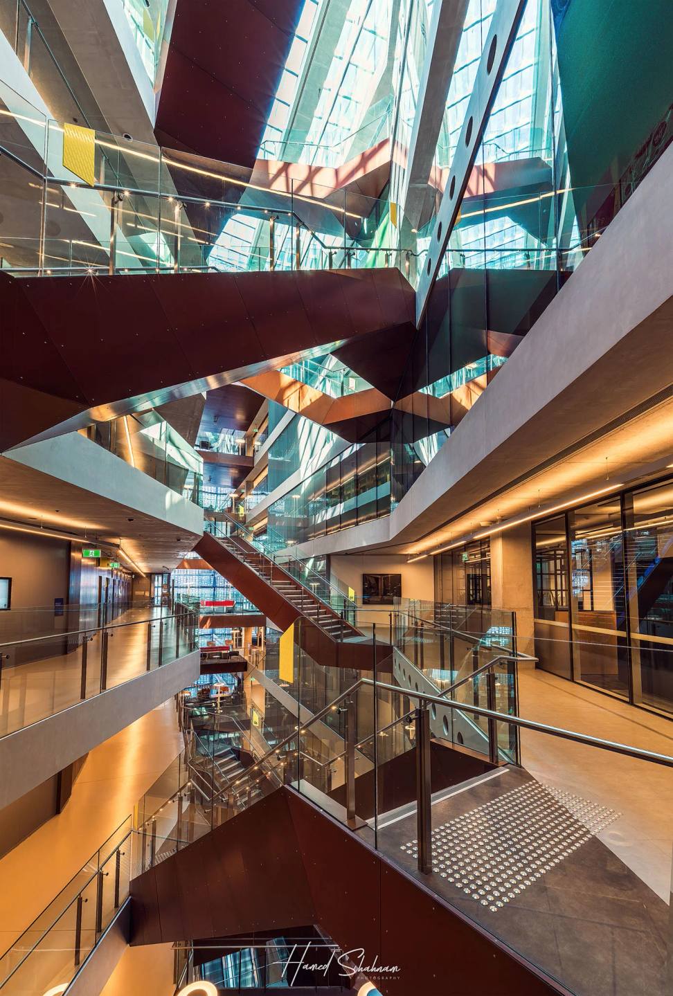 Intersecting staircases and reflections within a multilevel university interior.