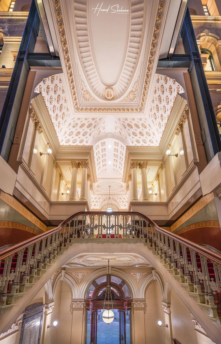 An ornate hotel staircase and balconies beneath a decorated vaulted ceiling.