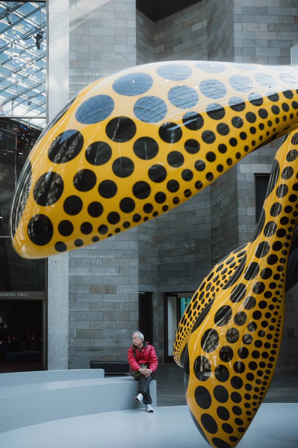A visitor beside a yellow sculpture patterned with black dots.
