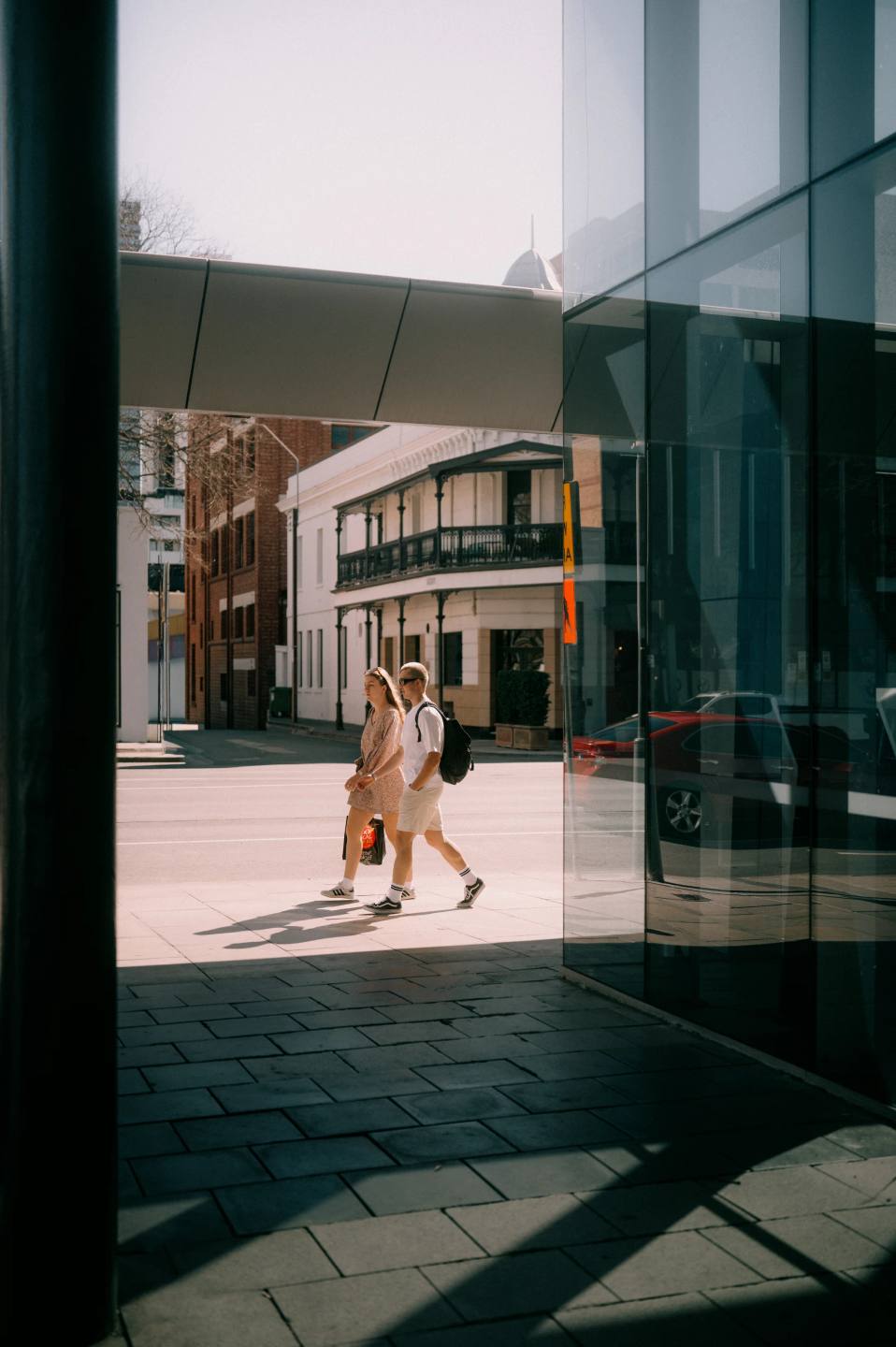 A pedestrian framed by glass and intersecting shadows.