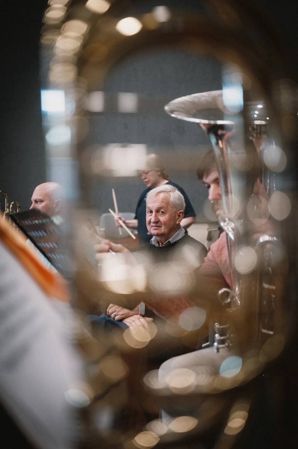 A seated orchestral musician framed by the curved tubing of a brass instrument. Australian Doctors Orchestra 2026, Adelaide.