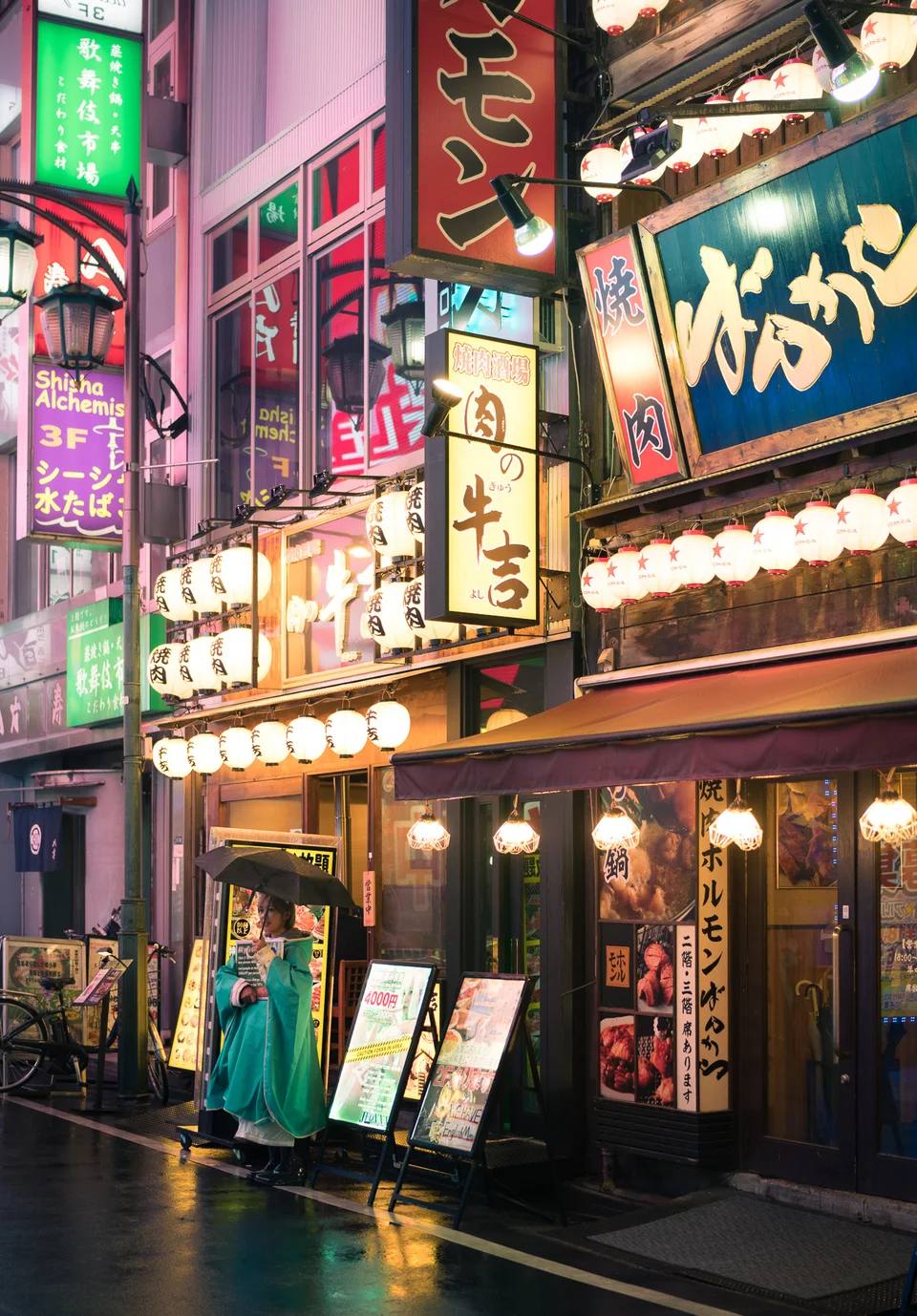 Colourful signs and reflected light along a narrow street at night.