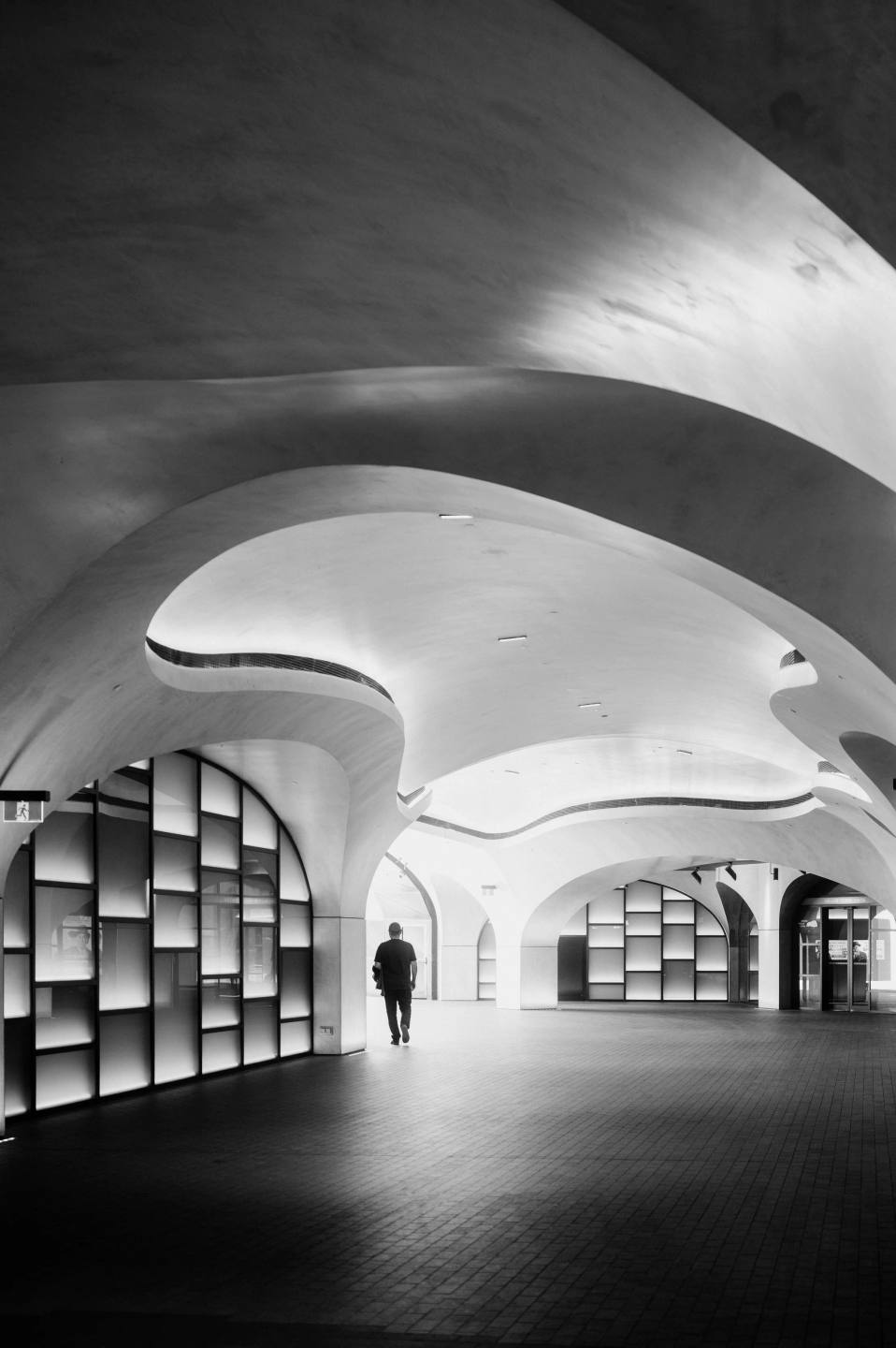 A lone figure beneath a sequence of sweeping concrete arches.