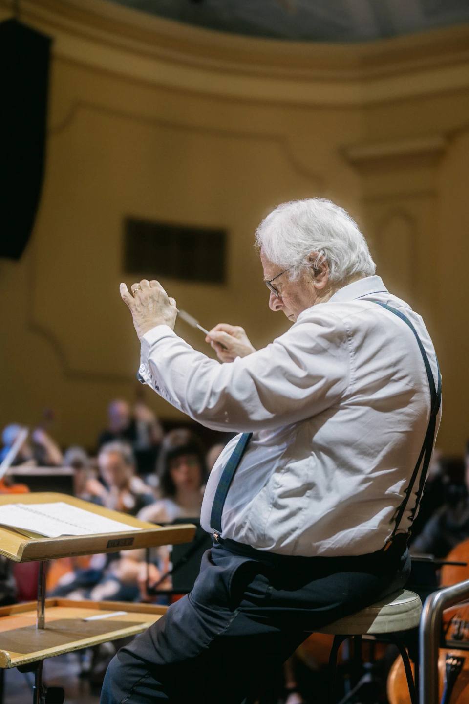 A conductor gesturing with raised hands beside a music stand. Australian Doctors Orchestra 2026, Adelaide.