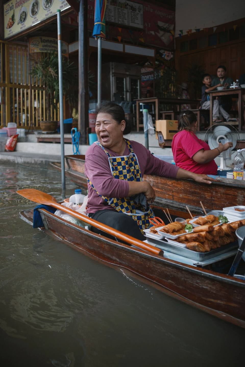 A smiling vendor preparing food from a wooden boat.
