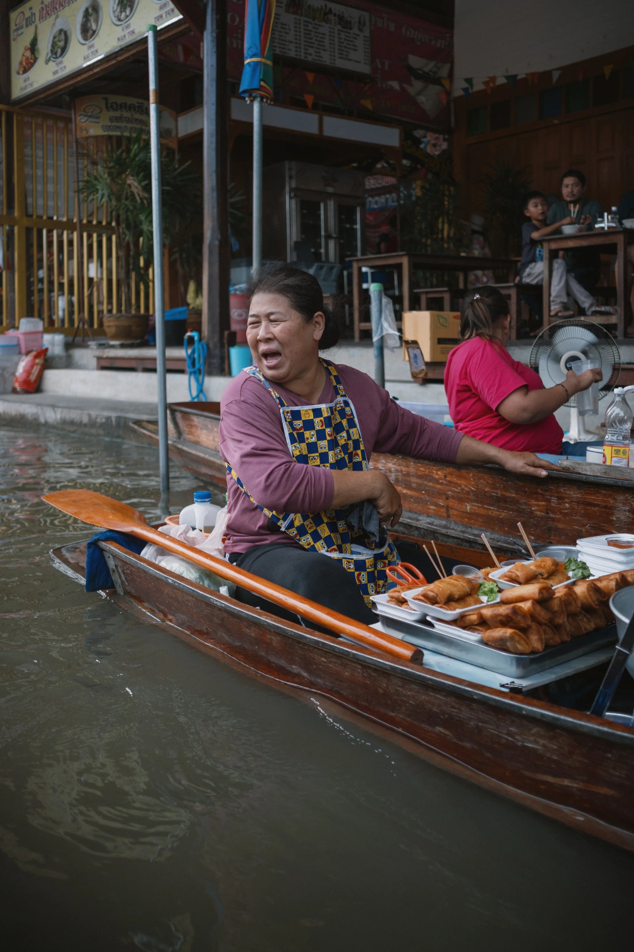 A smiling vendor preparing food from a wooden boat.