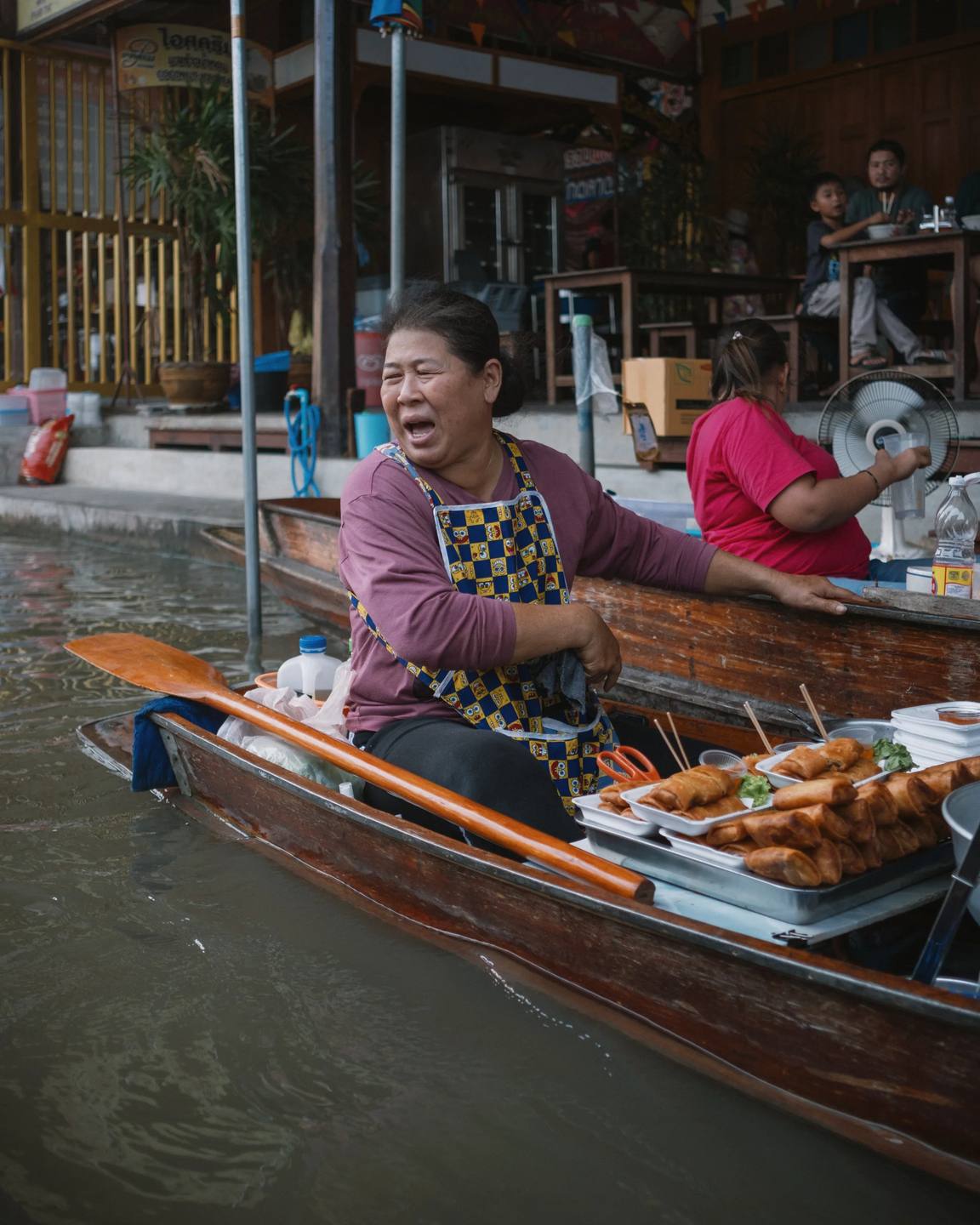 A smiling vendor preparing food from a wooden boat.