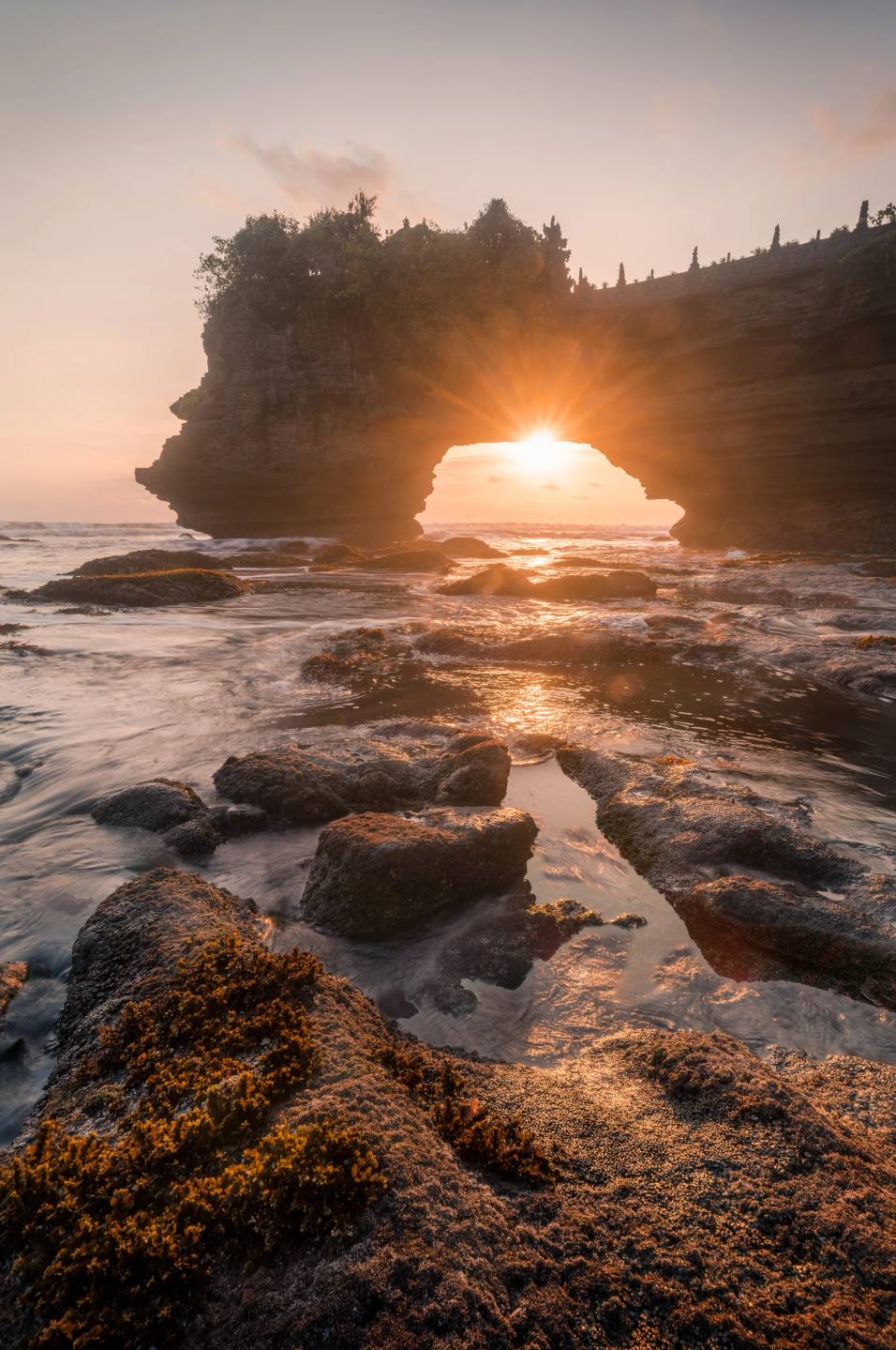 Sunset shining through a rocky coastal arch.