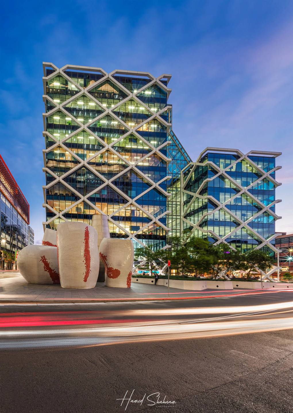 A contemporary glass building with diagonal framing above street light trails.