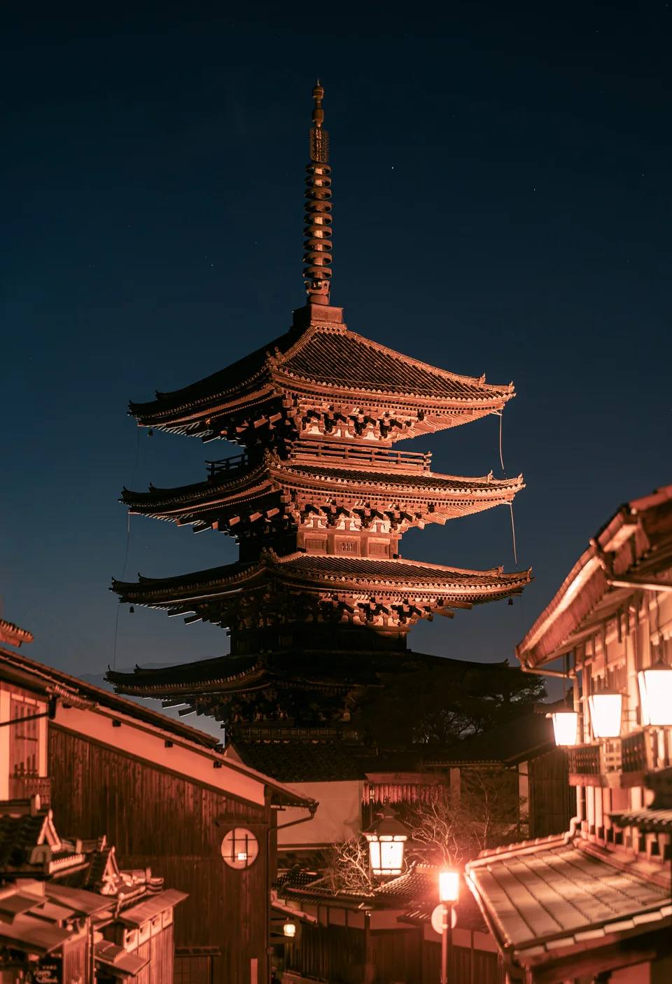A warmly illuminated pagoda above a narrow street at night.