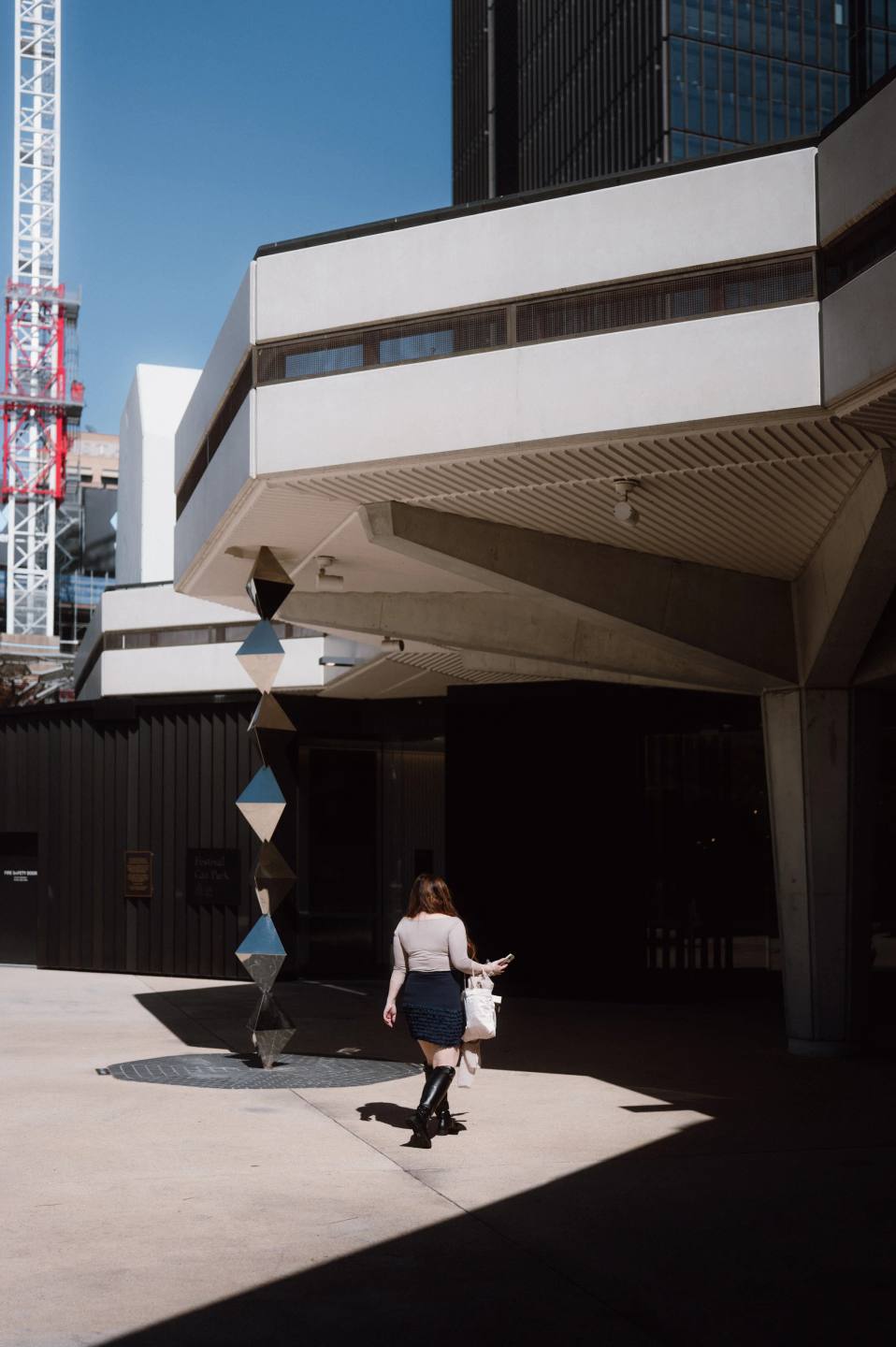A pedestrian crossing a patch of sunlight beneath an overhang.