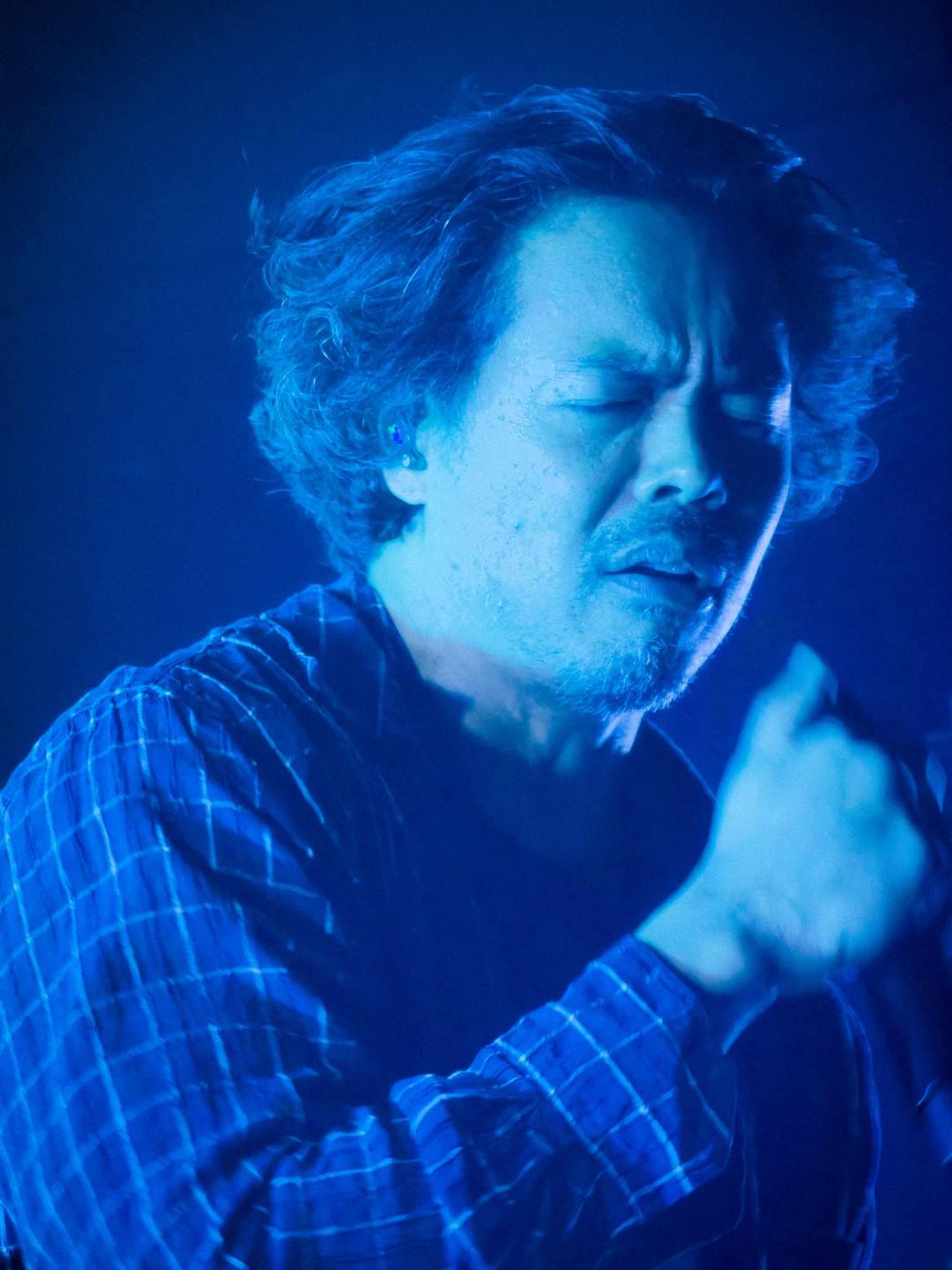 A close portrait of a singer with closed eyes holding a microphone under blue stage lighting.